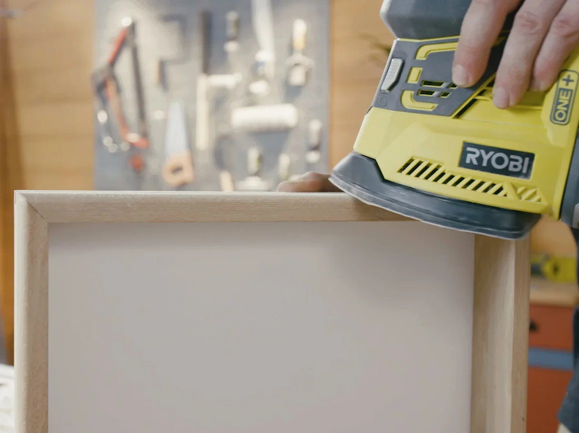 Person schleift Holzrahmen mit Schleifmaschine