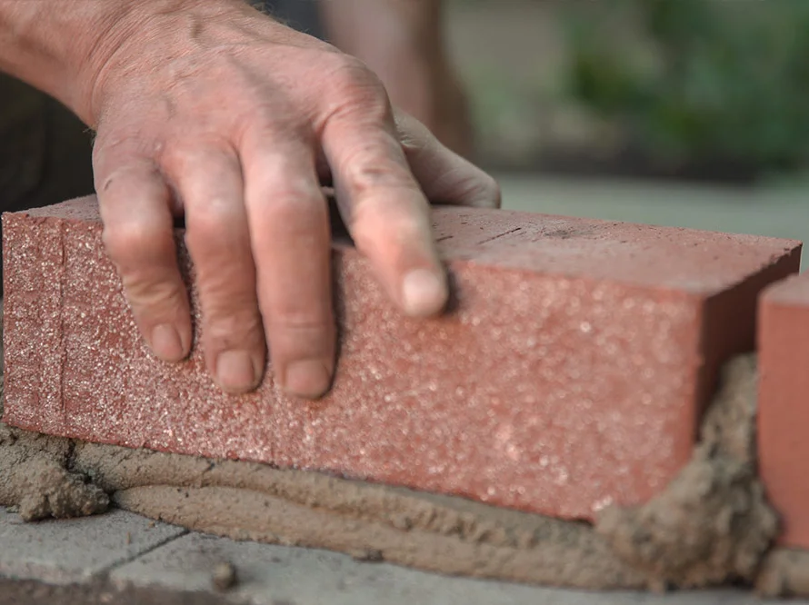 Hand setzt Ziegelstein auf Mörtel