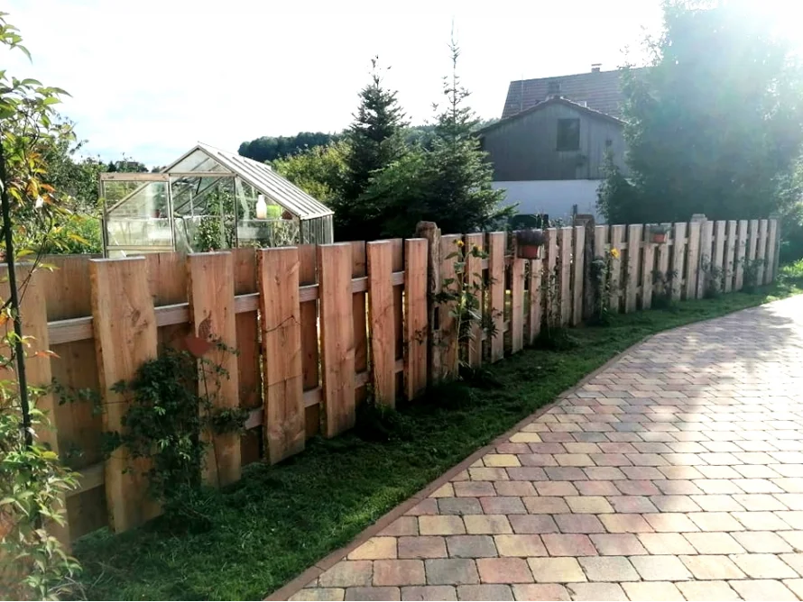 Gartenzaun aus Holz mit einem Gewächshaus im Hintergrund