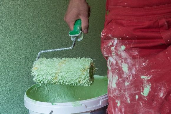 Ein Maler hält eine Farbwalze über einem Eimer mit grüner Wandfarbe.