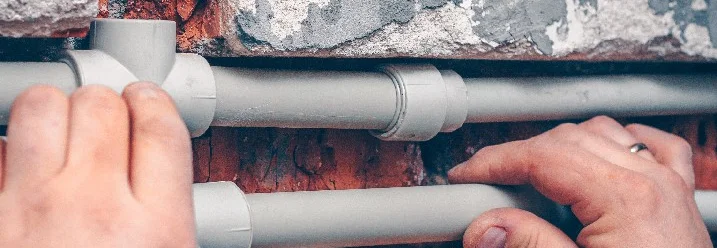 Hände befestigen Wasserrohre an einer Ziegelwand