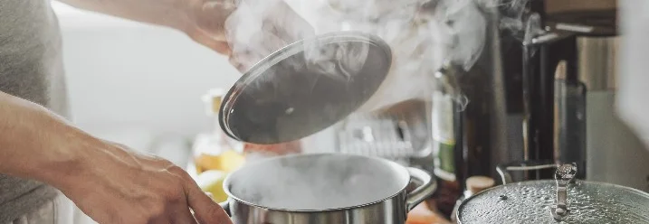 Person hebt Deckel von Topf auf Herd