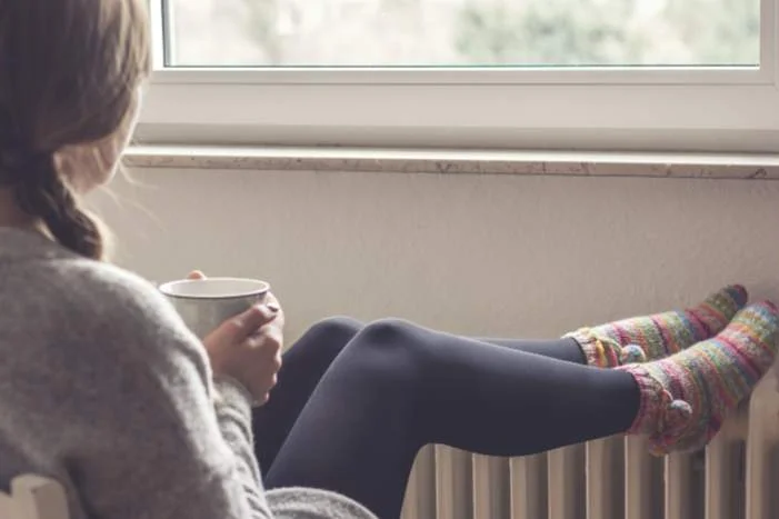 Person sitzt mit Tasse an Heizung