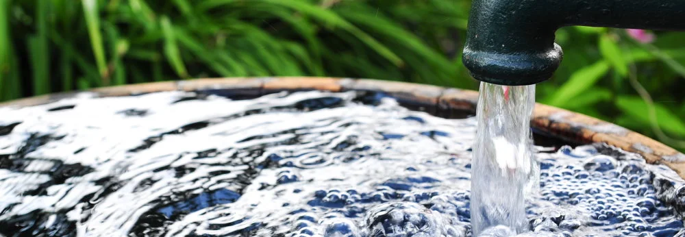Wasser läuft aus einem Hahn in ein Holzfass
