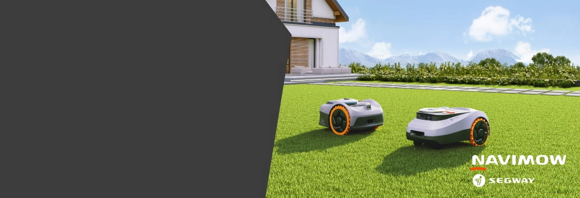 Zwei Mähroboter auf einer Rasenfläche vor einem Haus.