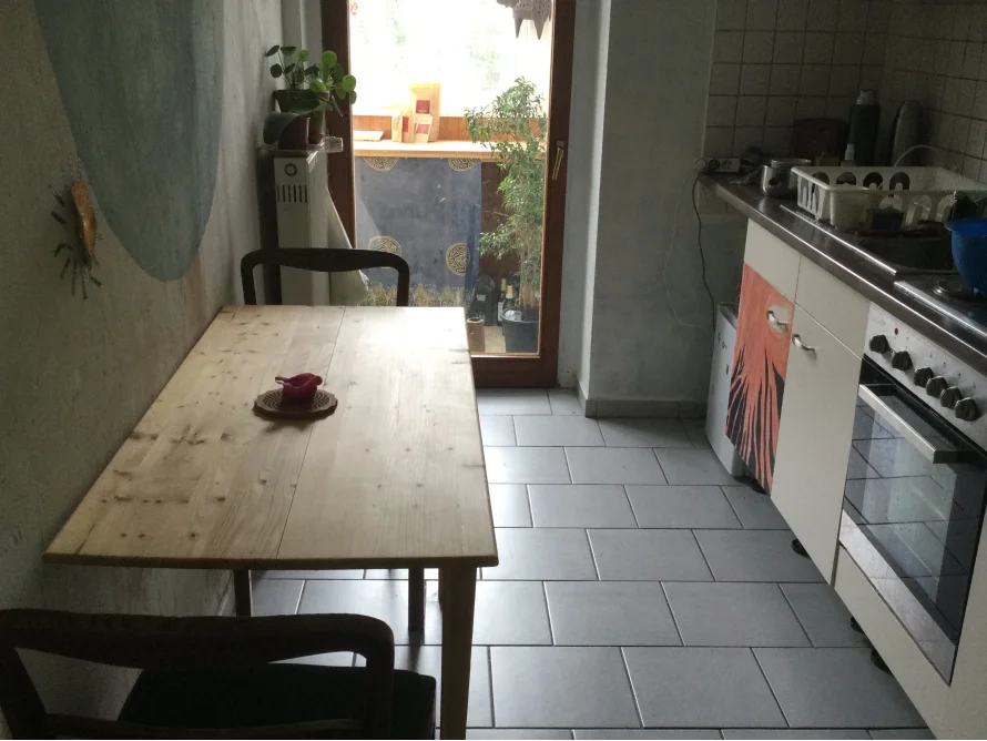 Ein heller Raum mit Esstisch und offener Küche.