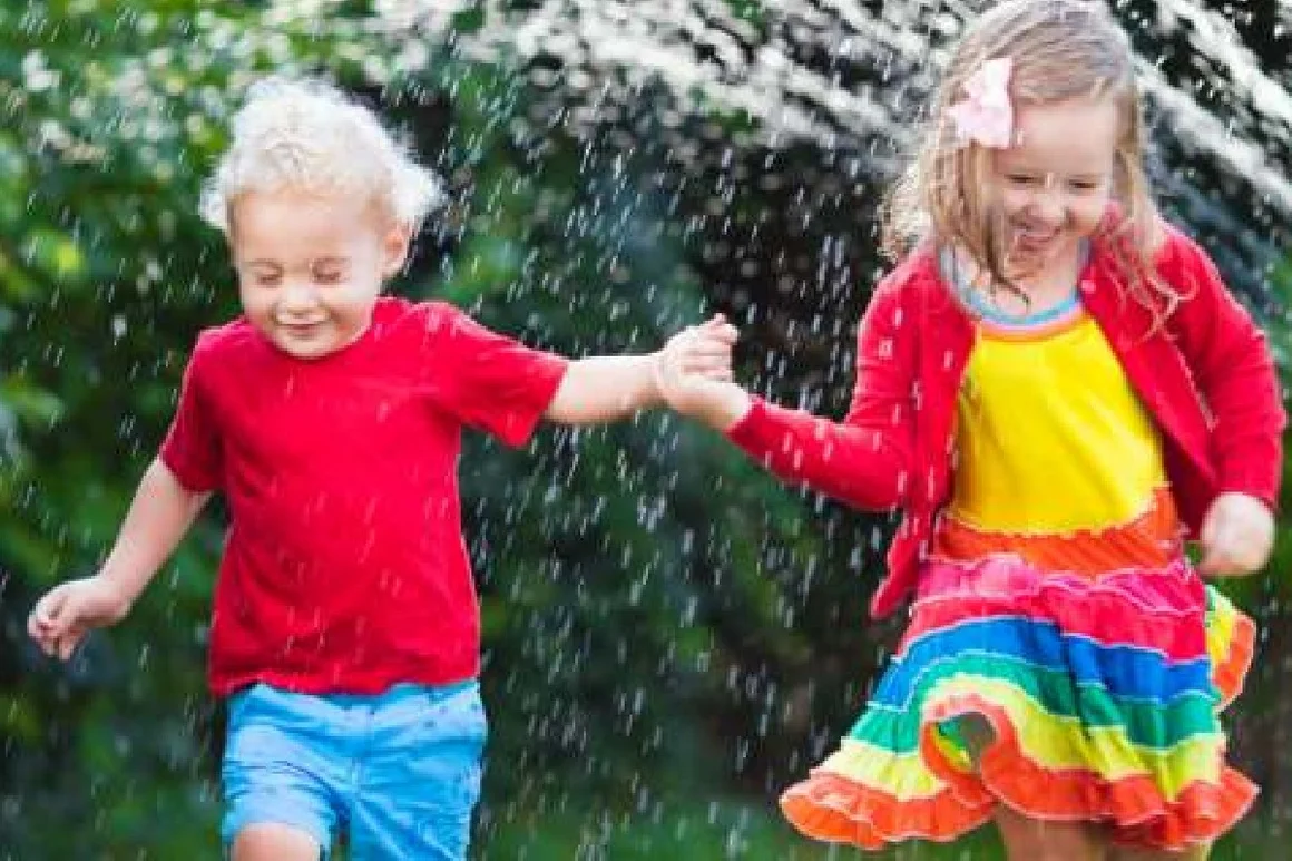 Zwei Kinder rennen durch einen Wasserstrahl