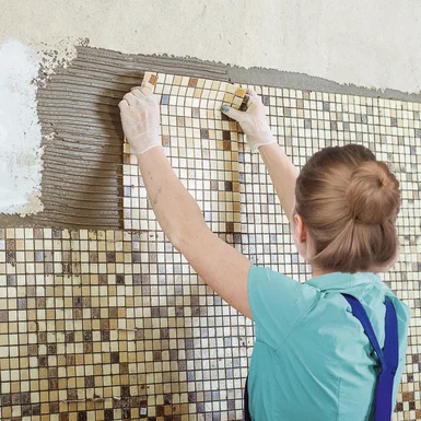Person verlegt Mosaikfliesen an einer Wand