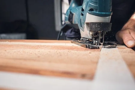 Person sägt Holzplatte mit Stichsäge