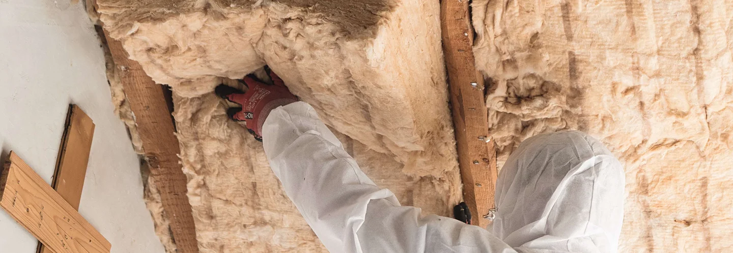 Person in Schutzkleidung beim Dämmen eines Dachs