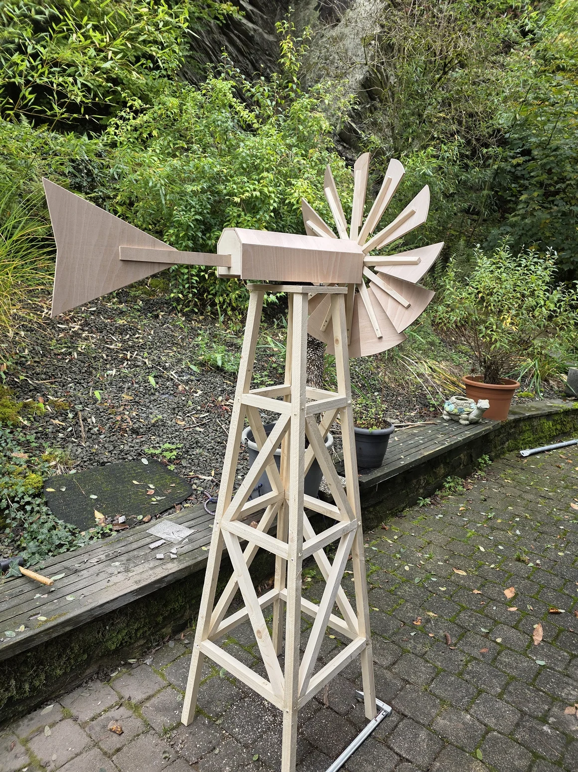 Eine selbstgebaute, unfertige Windmühle aus Holz steht im Freien auf einer Terrasse.