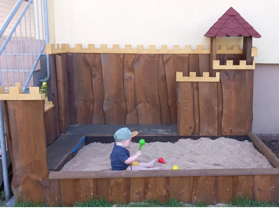 Kleinkind in einem Sandkasten aus Holz