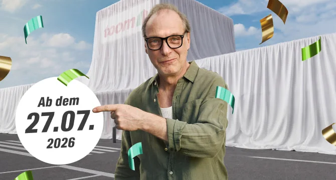 Mensch mit Brille zeigt auf ein Datum vor einem verhüllten Gebäude.
