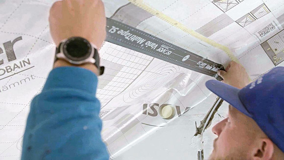 Mit Klebeband verklebt ein Handwerker Dampfbremsfolie im Dachstuhl.