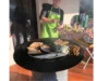 Person grillt Würstchen und Fisch auf einem Rundgrill