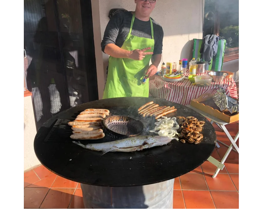 Person grillt Würstchen und Fisch auf einem Rundgrill
