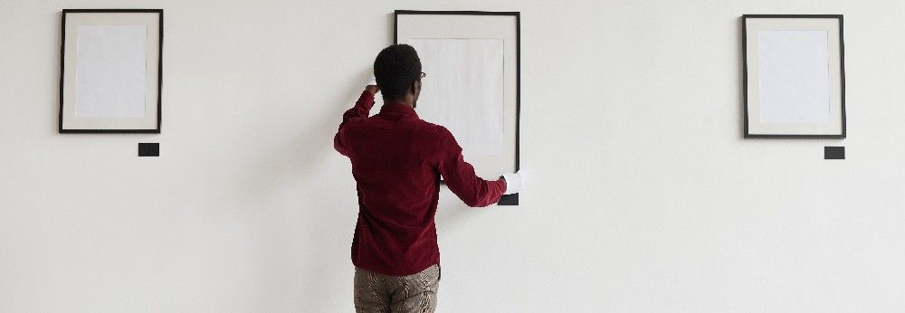 Ein Mann hängt Bilder in einer Galerie auf.