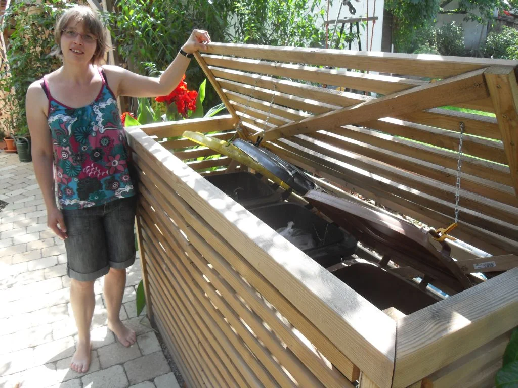 Person steht vor einem Mülltonnenhäuschen aus Holz