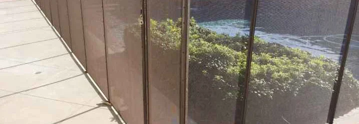 Ein mobiler, brauner Sicherheitszaun aus Netzstoff umgibt einen Pool.
