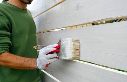 Mann streicht Holz mit weißer Farbe