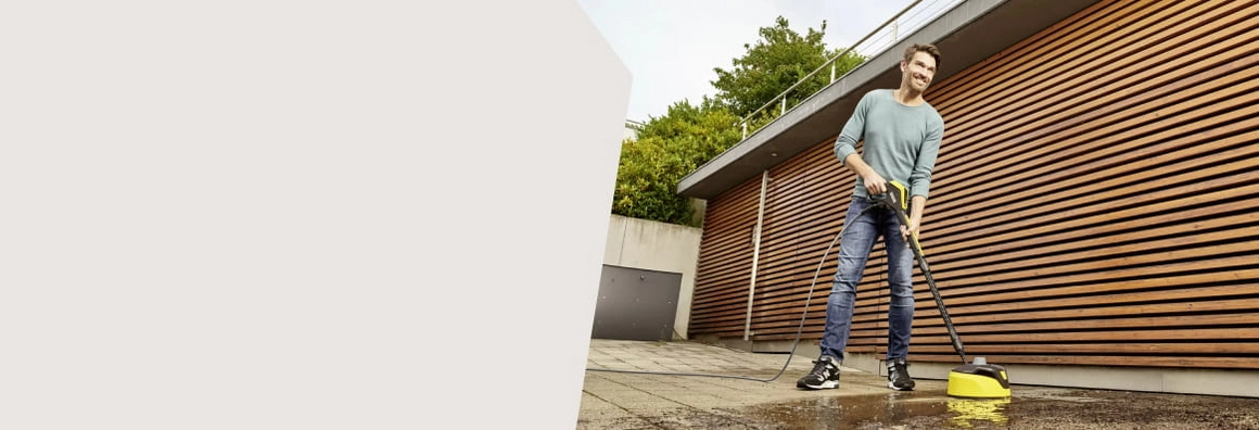 Eine Person reinigt eine Terrasse mit einem Hochdruckreiniger mit Flächenreiniger-Aufsatz.