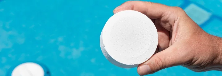 Hand hält Chlortablette über Pool