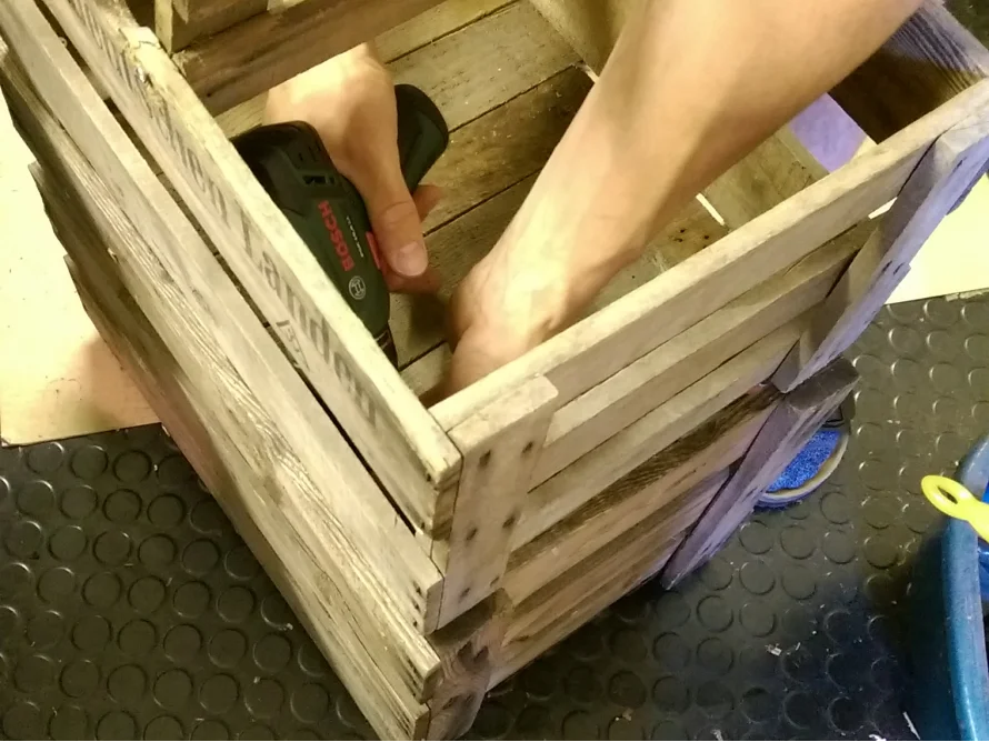 Person baut Holzkiste mit Akkuschrauber zusammen.
