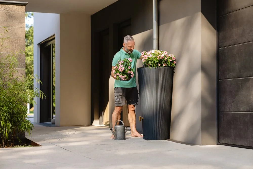 Person bepflanzt einen Regenwasserspeicher mit Blumen.