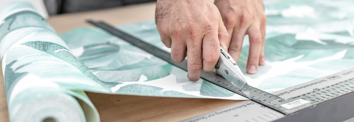 Person schneidet Tapete mit Cuttermesser