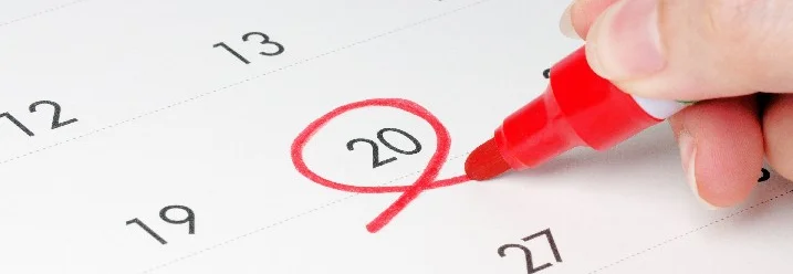 Hand markiert mit einem Stift den 20. Tag auf einem Kalender.