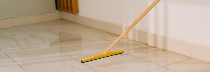 Person reinigt Fliesen mit einem Abzieher.