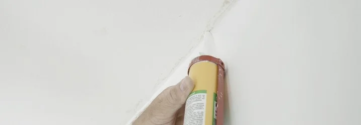 Person verwendet Dichtmittel in Deckenecke