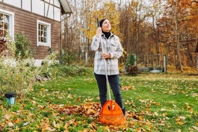 Eine Person steht mit einem Laubrechen in einem herbstlichen Garten.