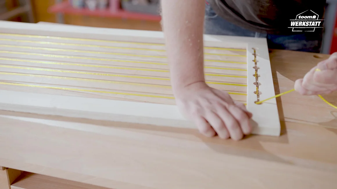 Person baut einen Holzrahmen mit gelber Kordel zusammen