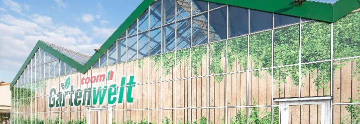 Außenansicht eines großen Gartencenters mit Glasfassade und grünem Dach.