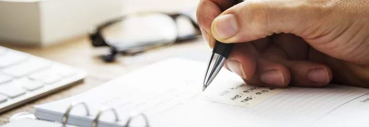 Hand schreibt mit Kugelschreiber in Notizbuch