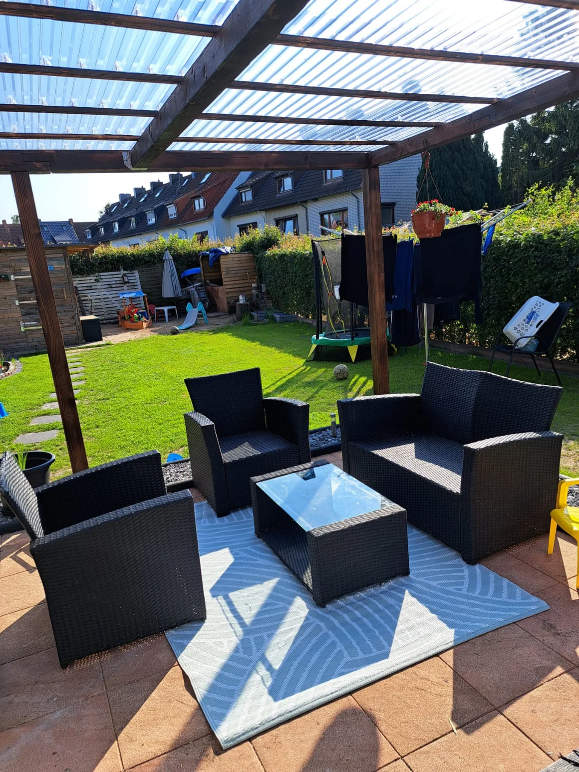 Schwarze Gartenmöbel auf einer Terrasse mit überdachter Pergola.