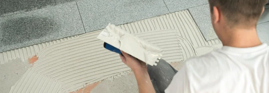 Person verlegt Fliesen mit Kleber