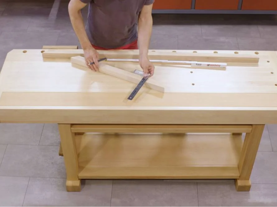 Person misst Holzlatten mit einem Winkel auf Werkbank aus