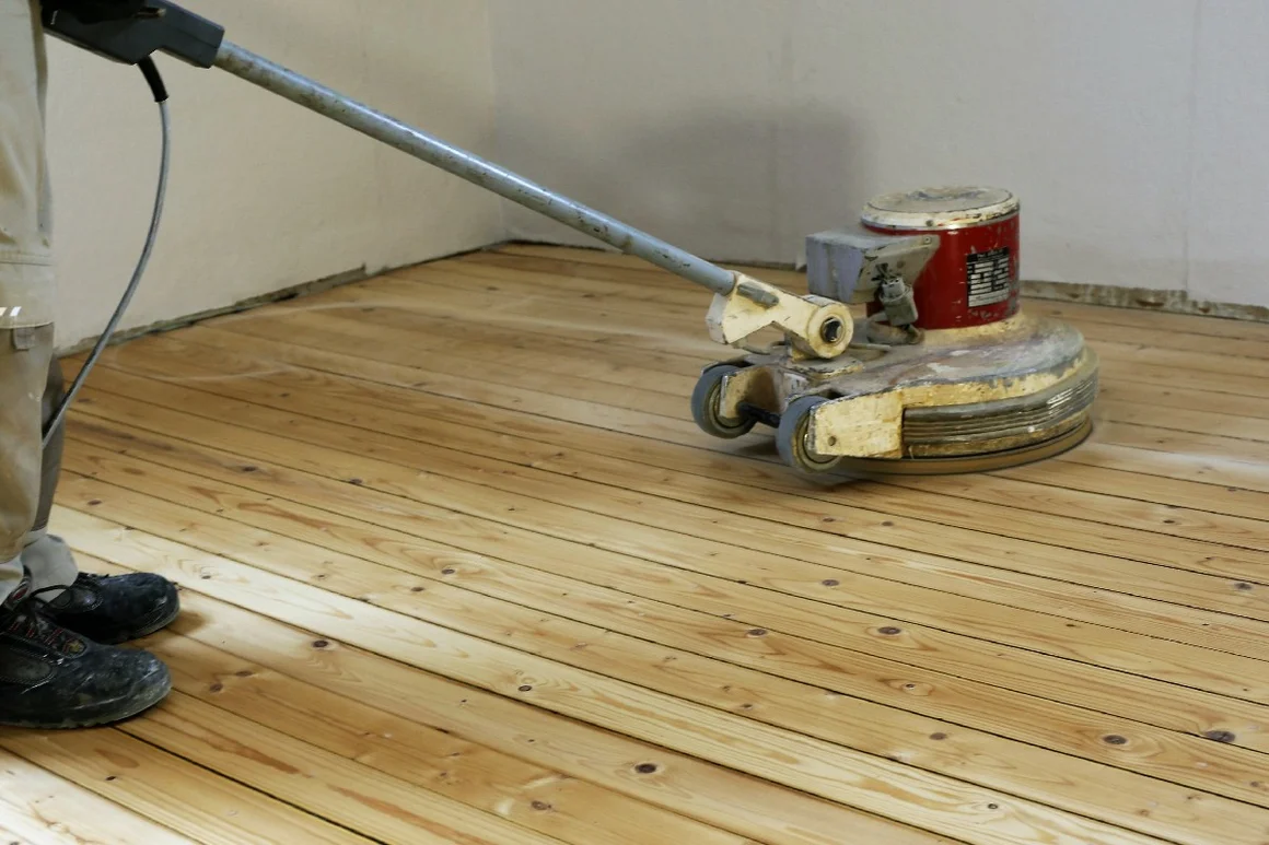 Person schleift Holzdielen mit Schleifmaschine
