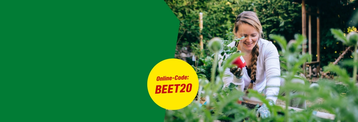 Eine lächelnde Person arbeitet in einem grünen Gartenbeet.