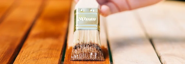 Person streicht Holzlatten mit Pinsel