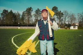 Platzwart steht mit Fahnen auf Fußballfeld