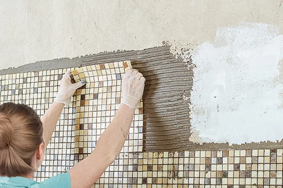 Person bringt Mosaikfliesen an Wand an