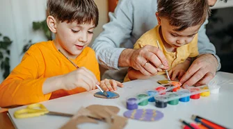 Zwei Kinder und eine erwachsene Person bemalen Pappfiguren mit Pinseln.