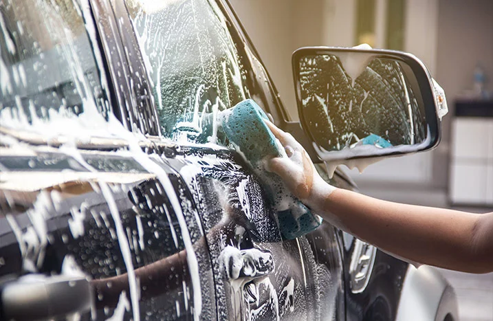 Person wäscht Auto mit Schwamm