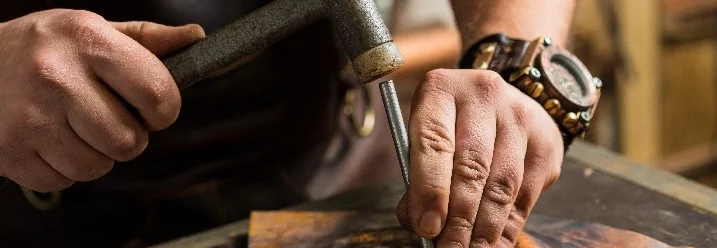 Person formt Metall mit Hammer und Meißel
