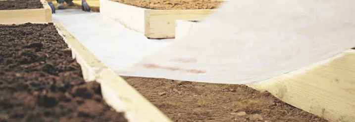 Person breitet Vlies in einem Hochbeet aus