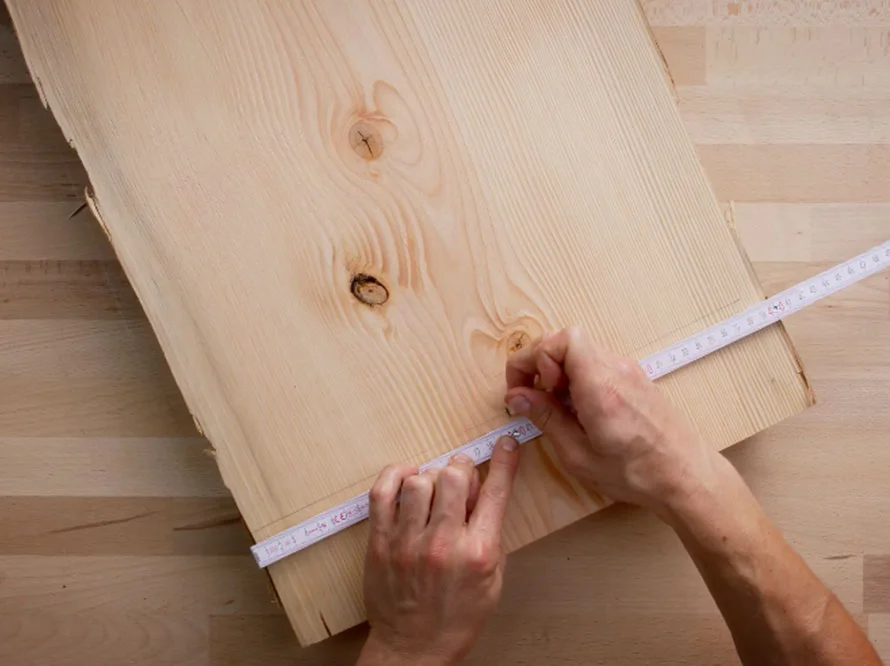 Person misst Holzbrett mit Zollstock ab