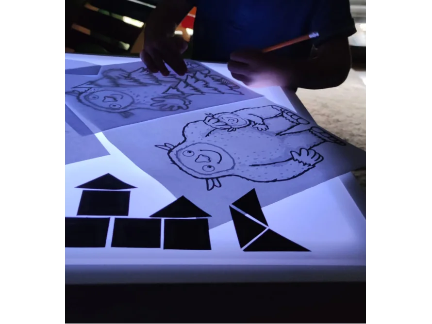 Person zeichnet ein Monster auf einem Leuchttisch mit Bleistift nach.